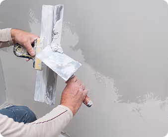 Handwerker trägt Putz mit Glättkelle auf eine Wand auf.